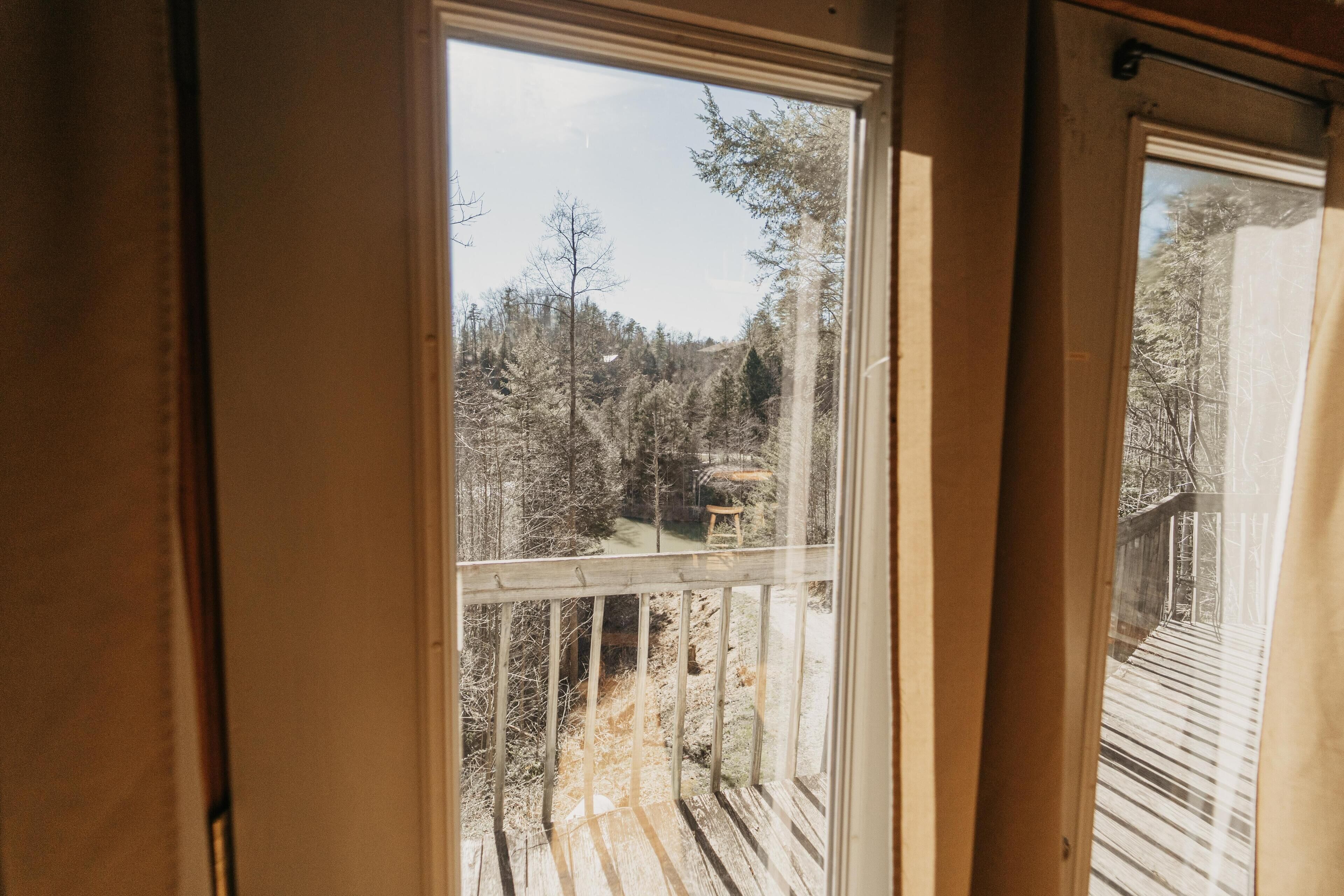 Une vue depuis une fenêtre donnant sur une terrasse en bois, avec en contrebas une zone boisée et un ciel dégagé.