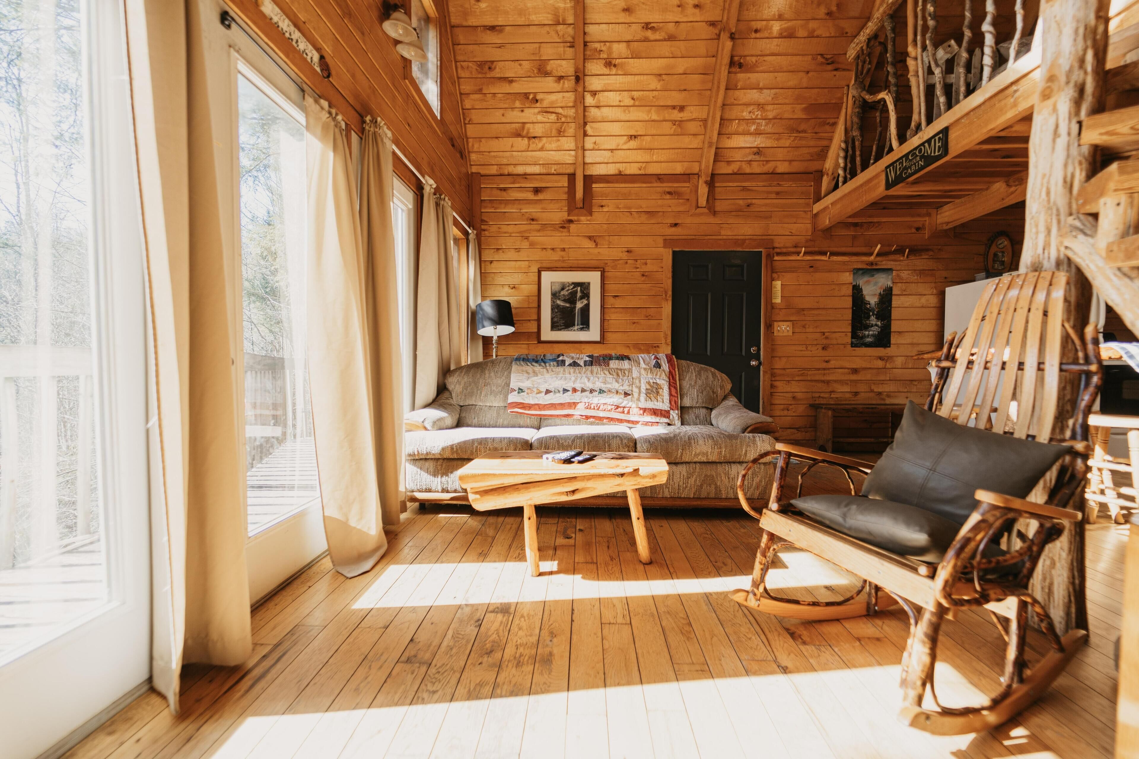 Un interior acogedor de cabaña con techo de madera, un sofá, un sillón mecedora y una mesita de centro.