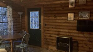 A cozy log cabin interior with a dining area, a fireplace, and a television.