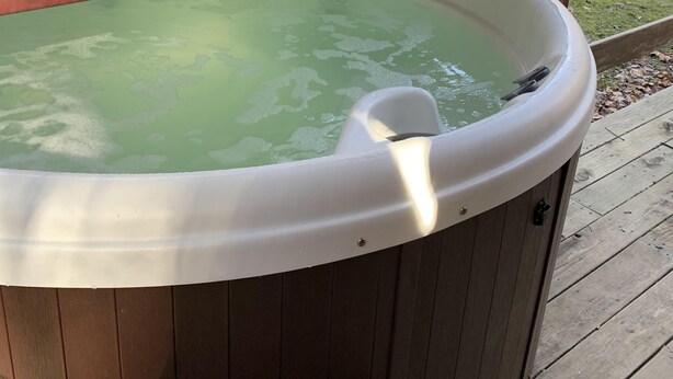 A hot tub with a wooden exterior and a white interior, situated on a wooden deck with a lattice fence in the background.