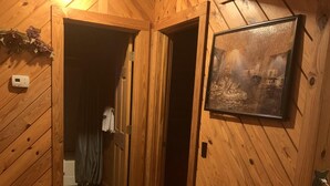 A wooden interior with a door leading to a bathroom, a thermostat, and a framed picture on the wall.