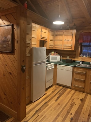 A wooden cabin kitchen with a refrigerator, stove, microwave, and sink.