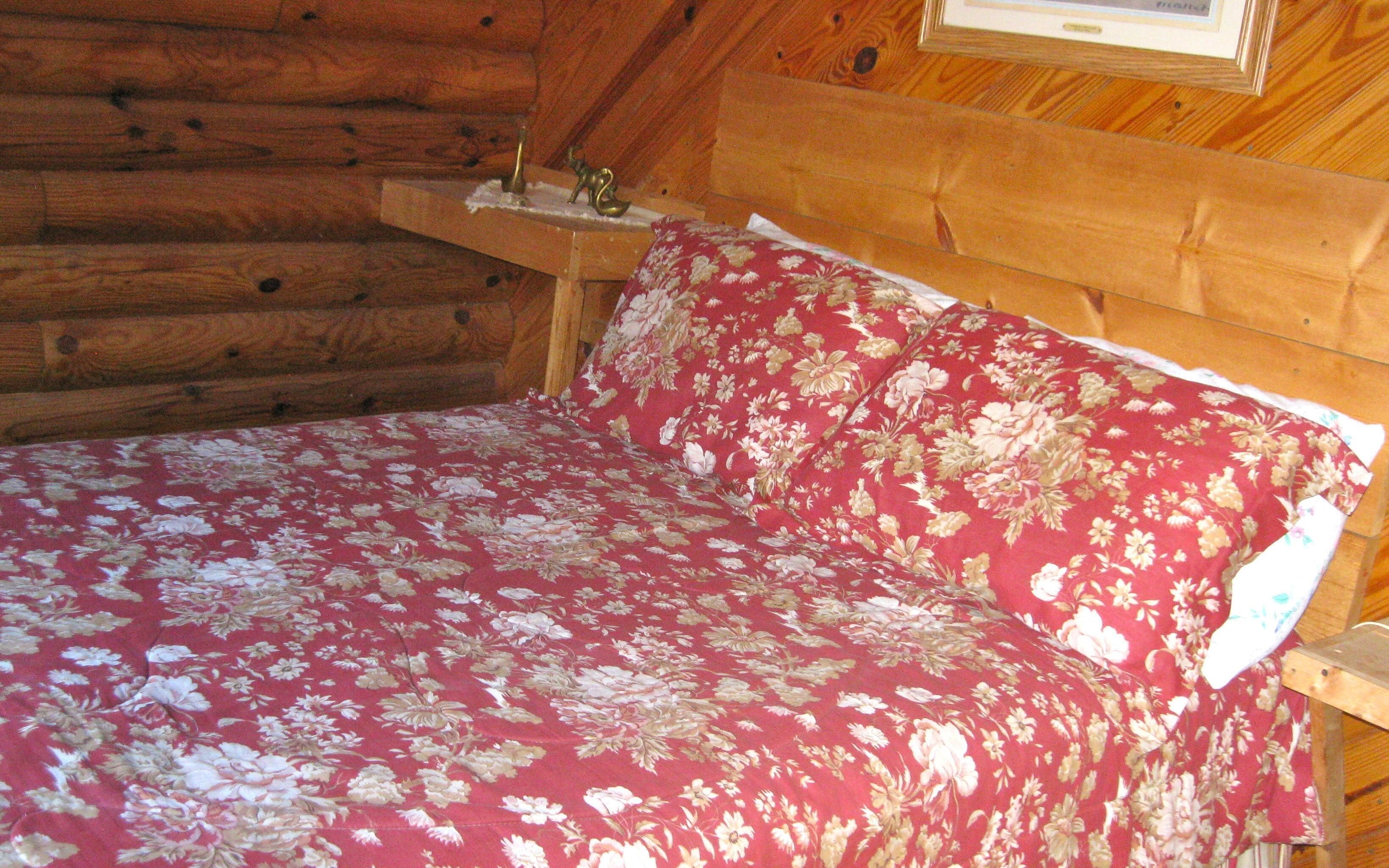A wooden cabin bedroom with a bed covered in floral bedding.