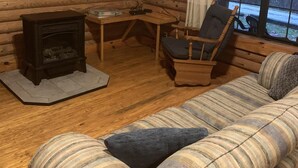 L’intérieur d’un chalet confortable, avec une cheminée, un téléviseur fixé au mur, une table en bois, une chaise et un canapé à rayures.