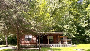 Une cabane en rondins avec une véranda, une petite terrasse et une clôture à treillis.