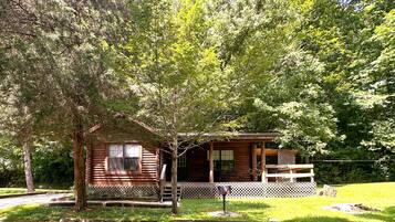 A log cabin with a porch, a small deck, and a lattice fence.