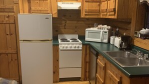 Une cuisine de taille réduite, dotée de meubles en bois, d’un réfrigérateur, d’une cuisinière, d’un four à micro-ondes et d’un évier.