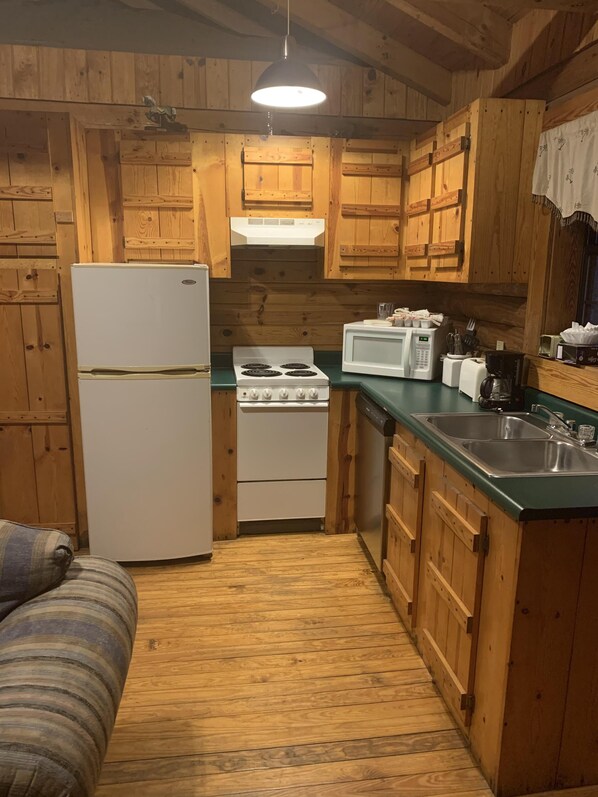 A compact kitchen with wooden cabinets, a refrigerator, a stove, a microwave, and a sink. - Log Cabin close to Natural Bridge State Park with hot tub and Wi-Fi (Slade)