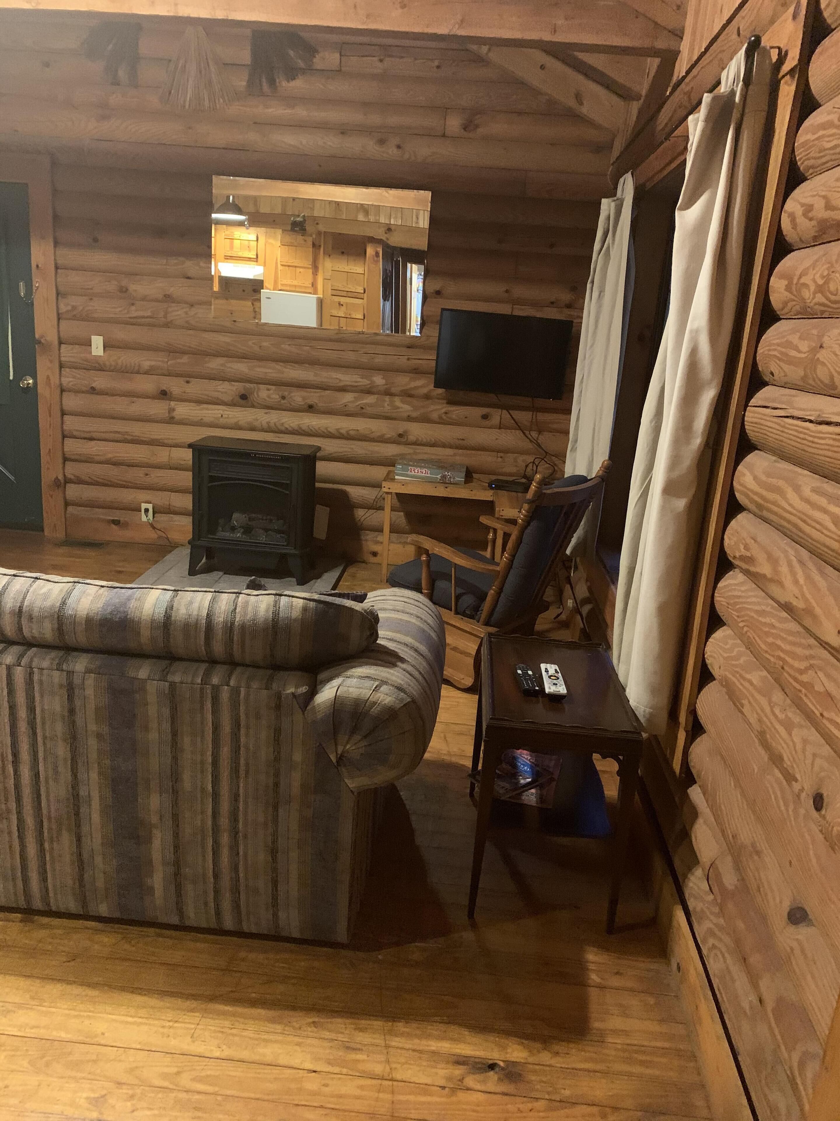 Interior acogedor de una cabaña de troncos con sofá, televisión y chimenea.