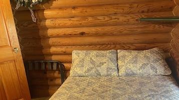 A wooden cabin interior with a bed, a door, and a wall-mounted wreath.