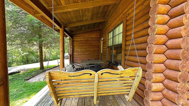 Une cabane en rondins avec une véranda, une balançoire et un coin repas.