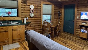 A cozy cabin-style room with a wooden interior, a dining table with chairs, a bench, a television, and a window with a view. - Cabin close to Natural Bridge State Park with hot tub and internet (Slade)