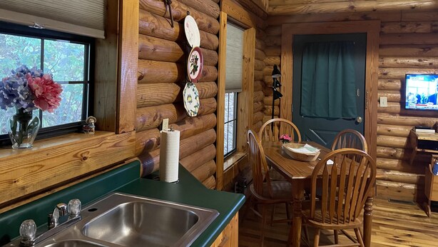 A wooden cabin interior with a kitchen area, dining table, and chairs. - Cabin close to Natural Bridge State Park with hot tub and internet (Slade)