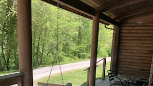 A wooden porch with a swing, a table with chairs, and a view of a forested area. - Cabin close to Natural Bridge State Park with hot tub and internet (Slade)
