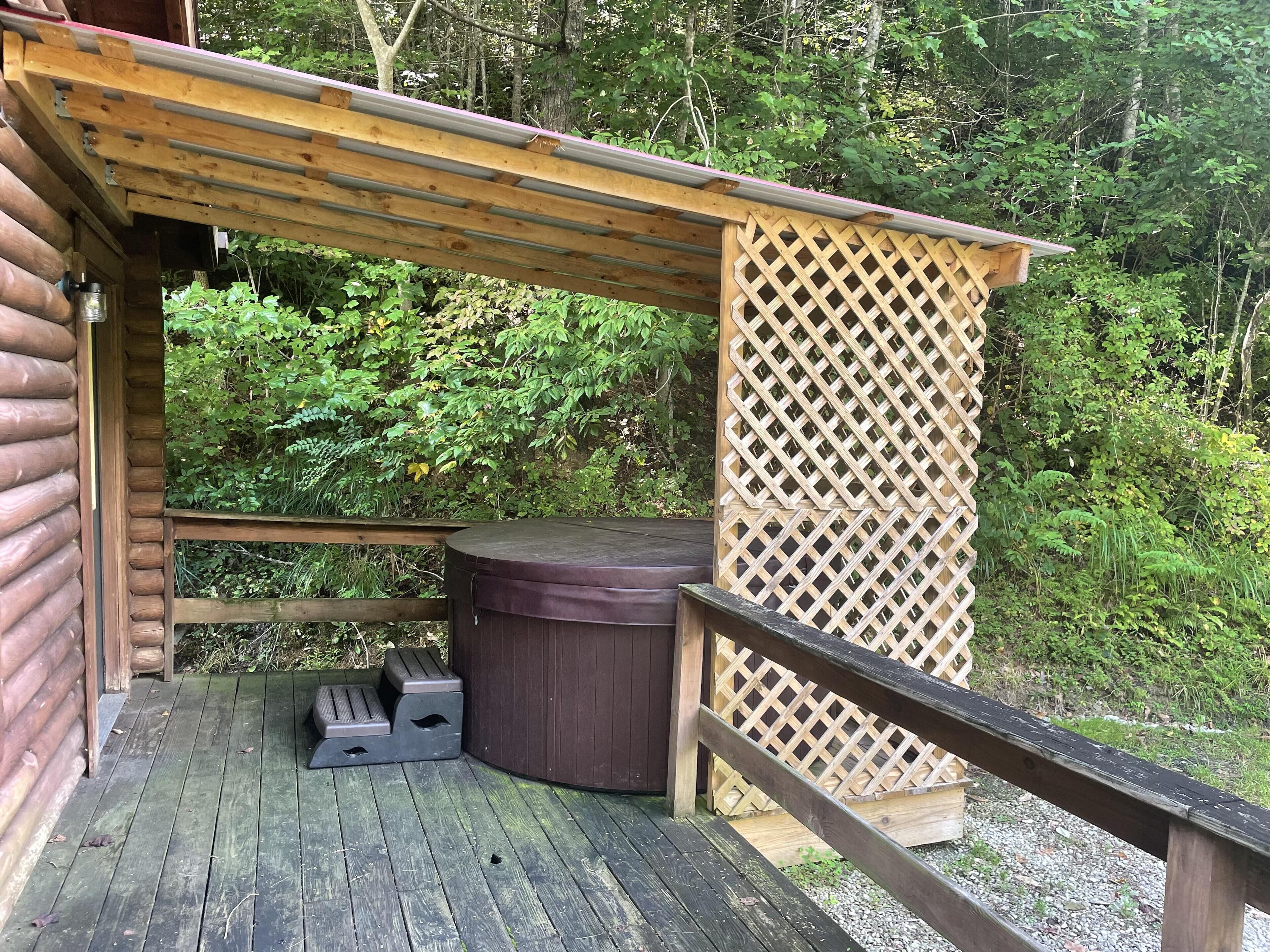 A wooden deck with a hot tub, a wooden fence, and a view of dense greenery.