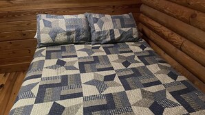 A bed with a geometric patterned quilt and matching pillows in a log cabin-style room. - Cabin close to Natural Bridge State Park with hot tub and internet (Slade)