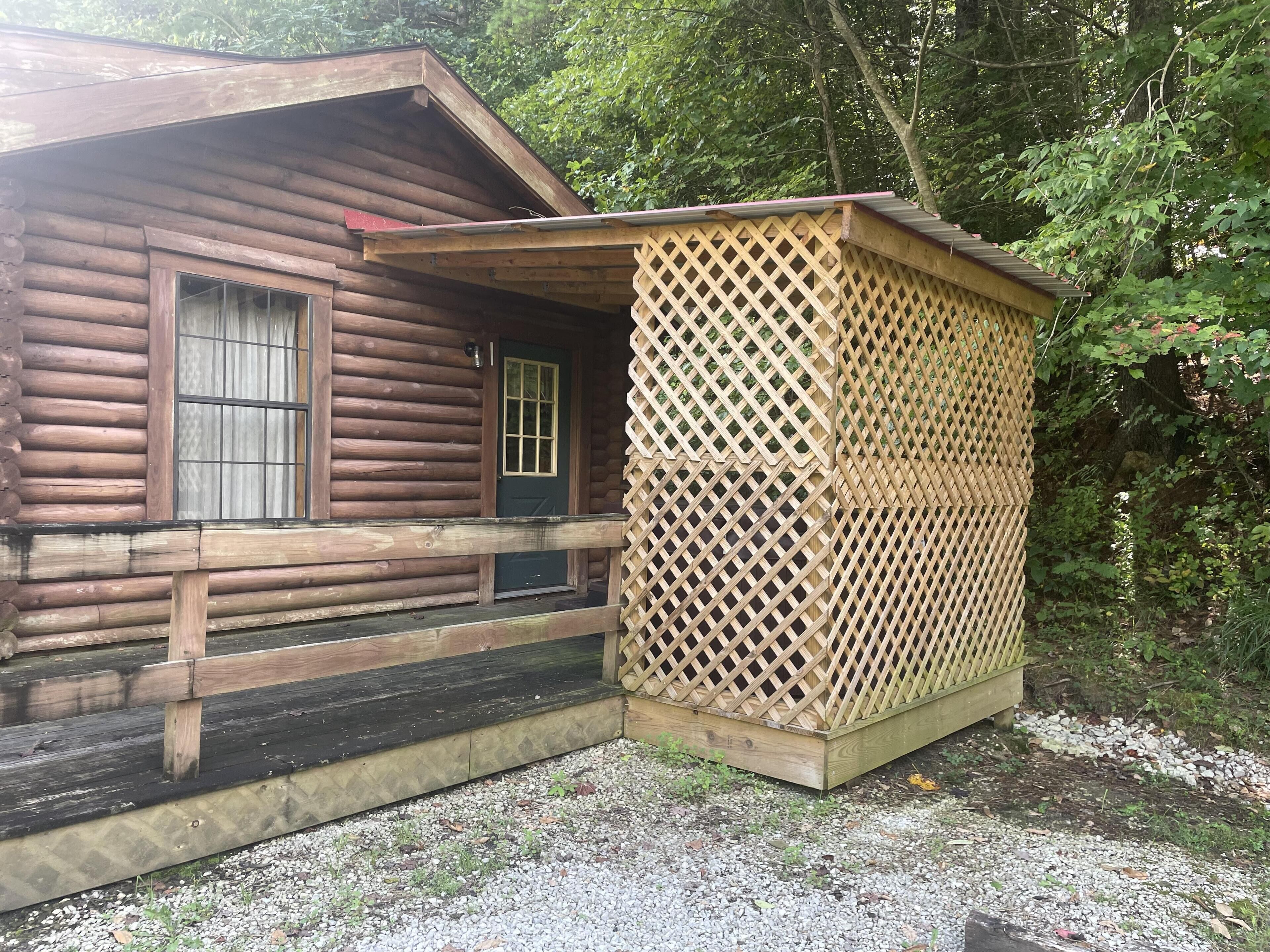 A wooden cabin with a porch and a lattice-covered structure.