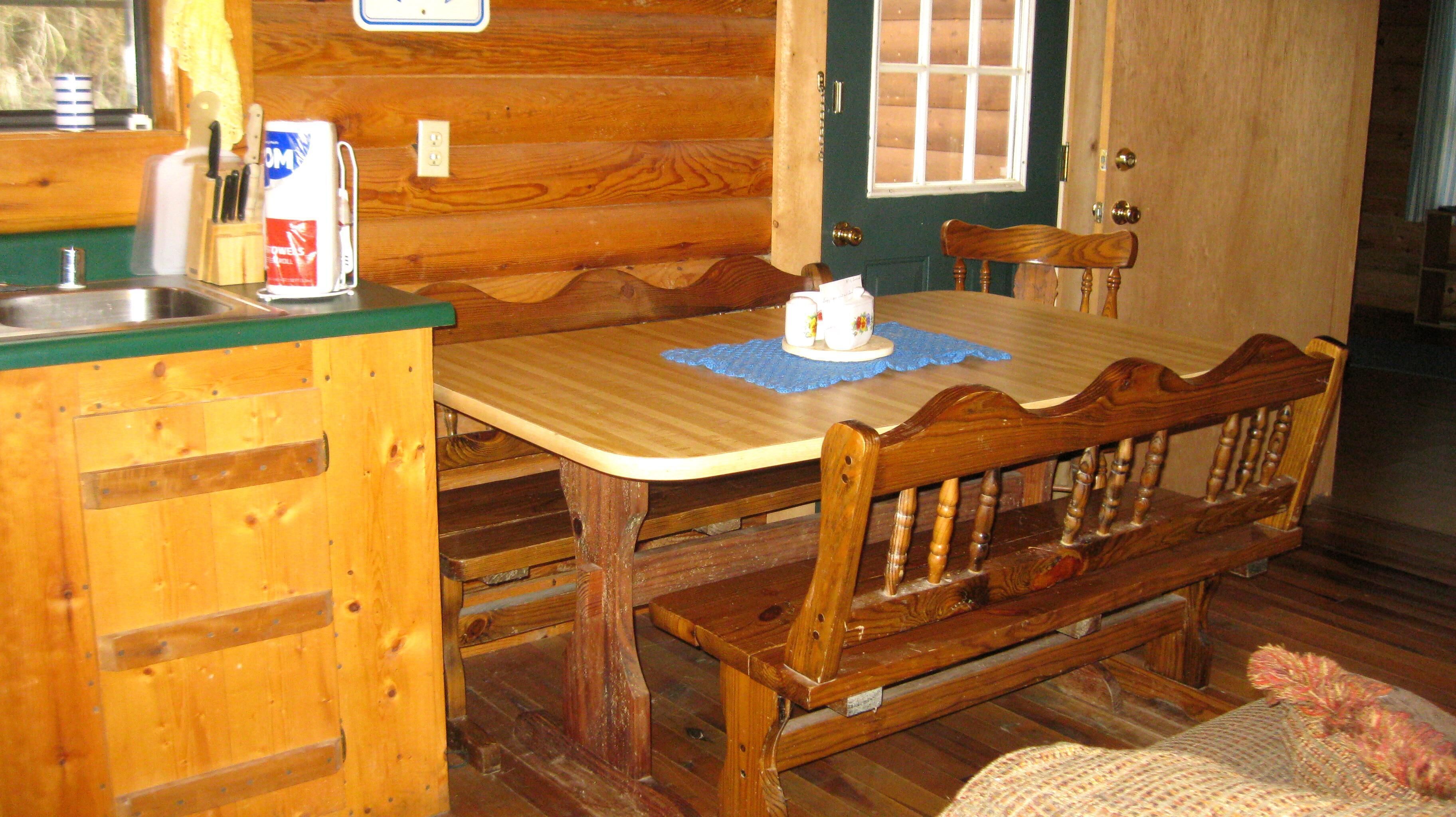 L’intérieur d’une cabane en bois comprend un coin cuisine, une table à manger et un banc.