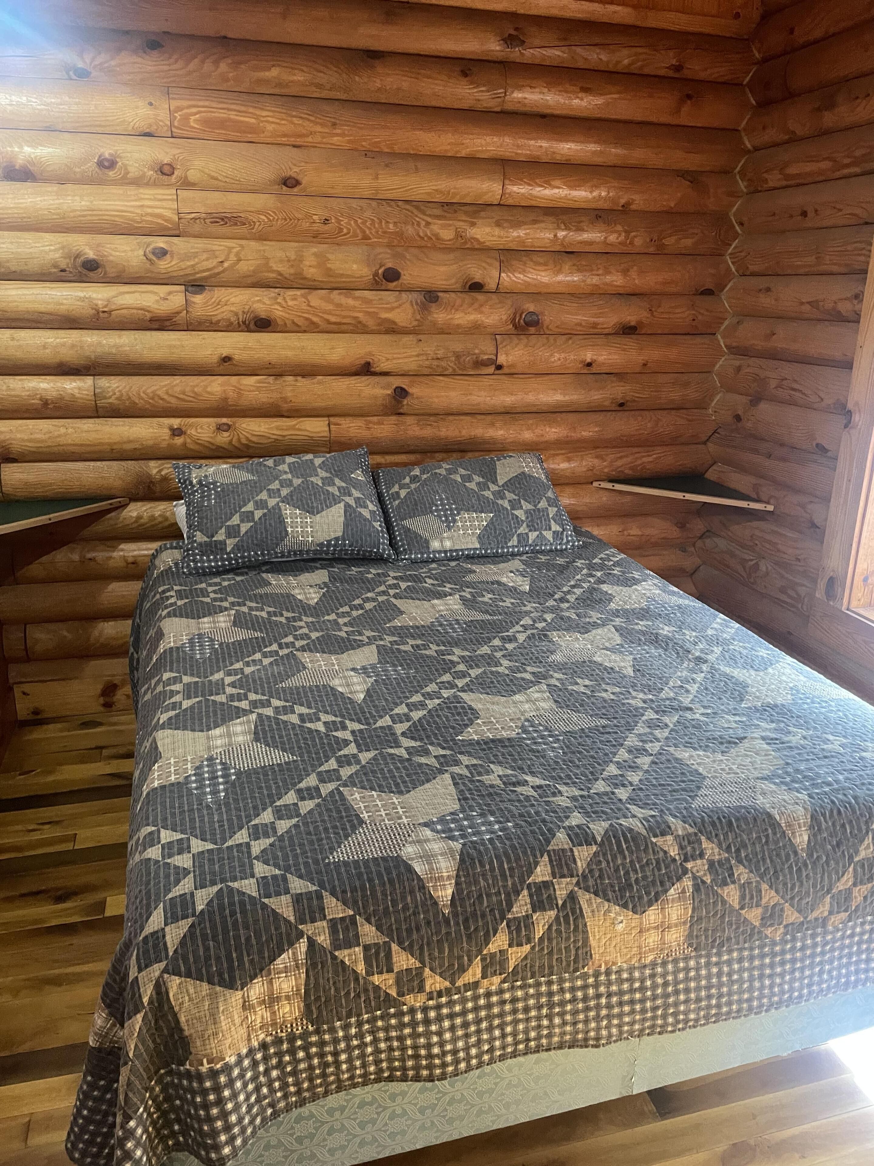 Une chambre aménagée dans un chalet en rondins, avec un lit, des oreillers et une petite étagère.