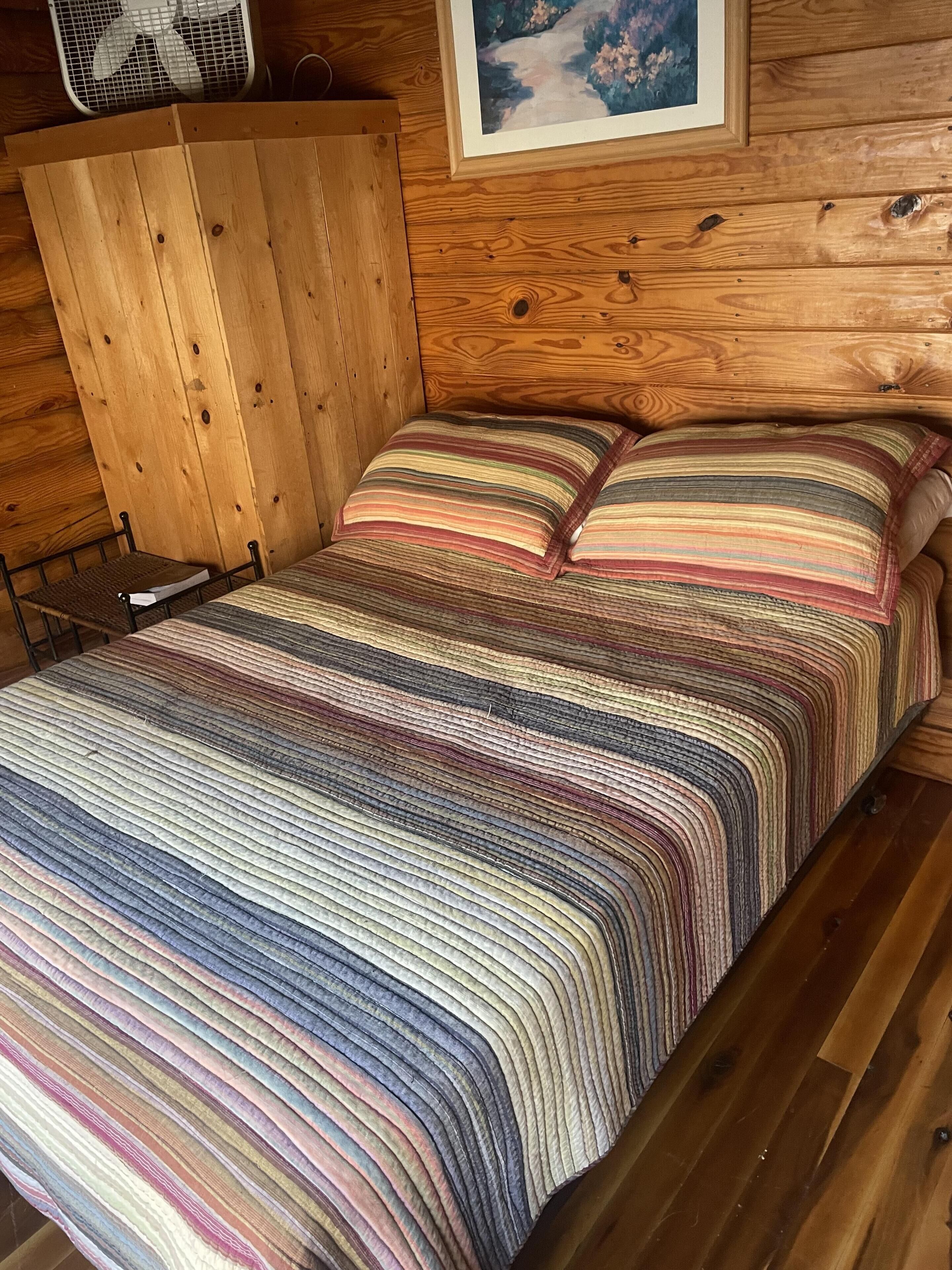 A wooden cabin-style room with a bed, a wooden wardrobe, and a framed picture on the wall.