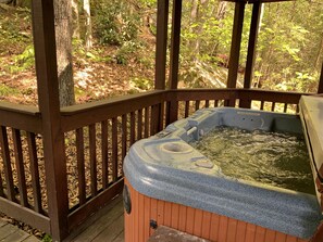 A hot tub with a wooden deck and a wooden railing, surrounded by trees.