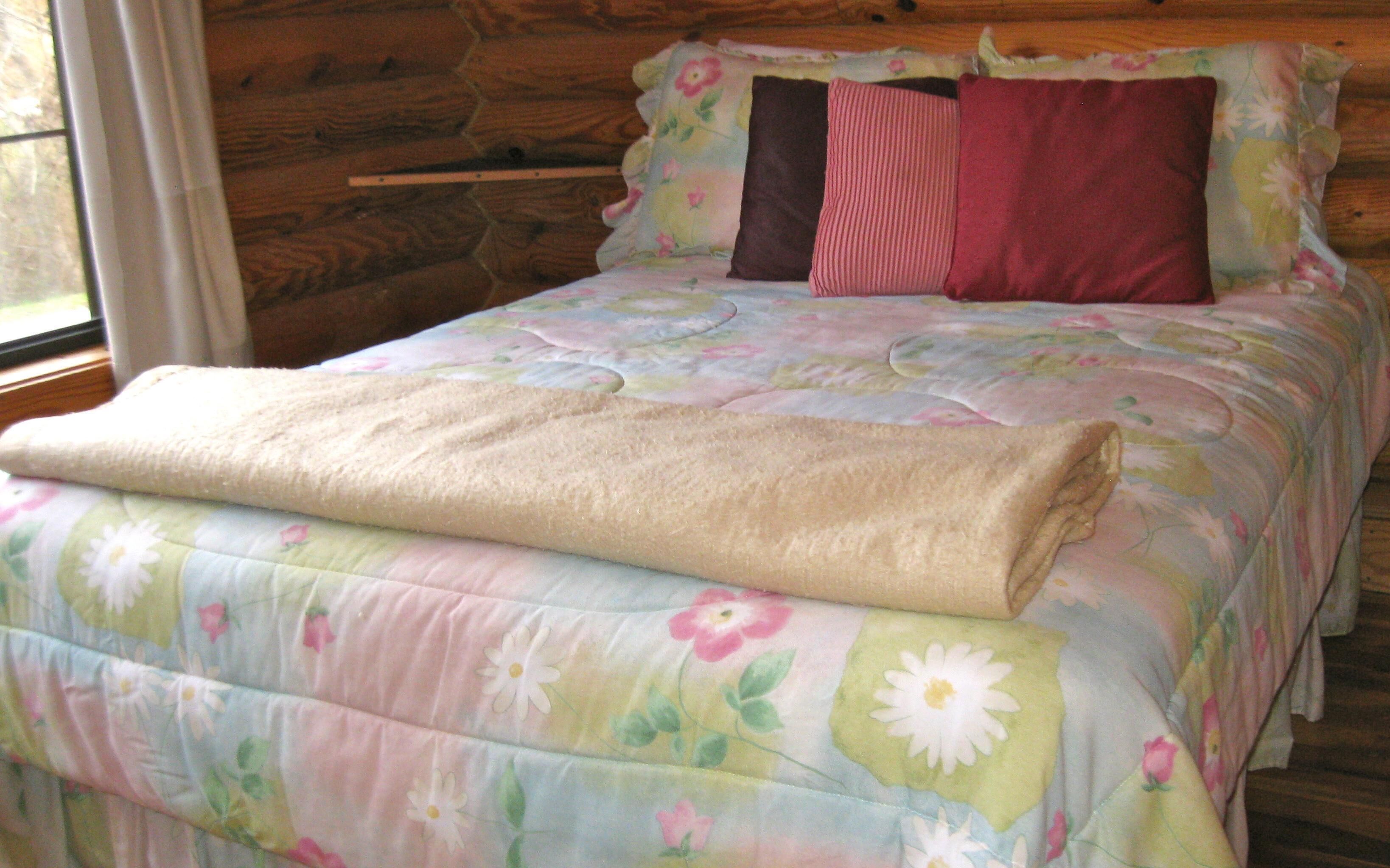 Ein Bett mit einer blumigen Bettdecke, einer gefalteten Decke und zwei Kissen.