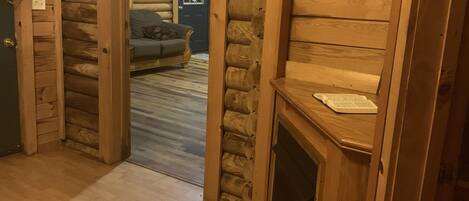Un interior de fusta amb una llar de foc, un sofà i una porta que dona a una altra habitació.