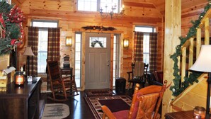 A cozy log cabin interior with a wooden ceiling, a central door, and a staircase with a garland. - Spacious cabin with Hot Tub and wood burning fireplace and wi-fi (Campton)