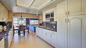 A modern kitchen with white cabinets, a stainless steel microwave, and a dining area with a blue sofa and chairs.
