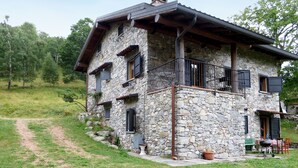 Une maison en pierre avec un balcon, un chemin menant à celle-ci et un petit espace extérieur aménagé pour s’asseoir.