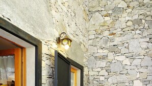 Une pièce aux murs de pierre, avec un fauteuil en osier et une porte en bois.