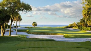 Un campo de golf con búnkeres de arena y árboles, con vistas al océano.