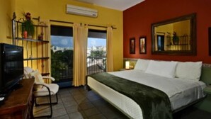 A hotel room with a bed, a desk with a computer, a chair, a TV, a window with curtains, and a balcony. - Summer Place Inn Full House (San Miguel Cozumel)