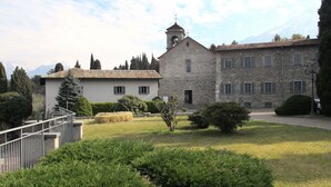 Un edificio de piedra con un campanario, rodeado de jardines cuidados y un cielo despejado.