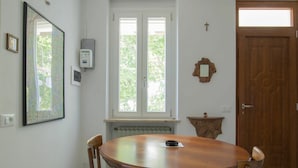 Comedor con mesa redonda de madera y cuatro sillas, ventana con vistas a zonas verdes, radiador debajo de la ventana y puerta de madera.