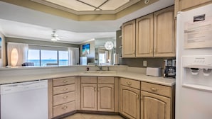 A modern kitchen with wooden cabinets, a dishwasher, a refrigerator, and a window with a view of the ocean. - Gulf Views & Pool Access: Coral Reef Resort Condo (Panama City Beach)