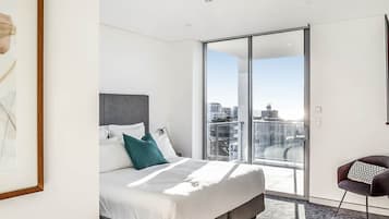 Quarto de hotel moderno com uma cama grande, vista da cidade através de uma porta de vidro deslizante e uma obra de arte emoldurada na parede.