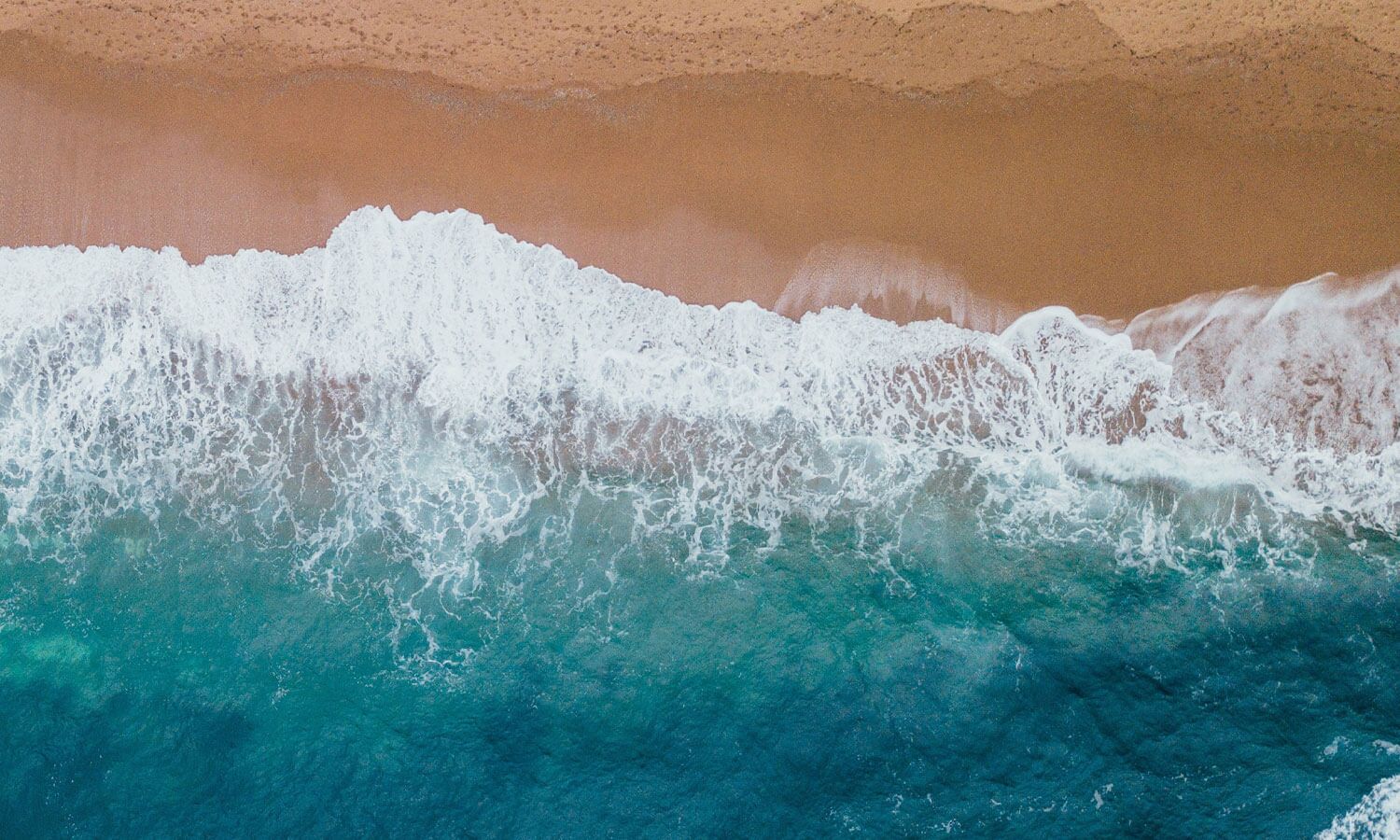 An aerial view of a beach with waves crashing onto the shore.