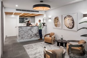 A modern reception area with a marble counter, seating with leather upholstery, and abstract wall art. - Argo Serviced Apartments (Wollongong)