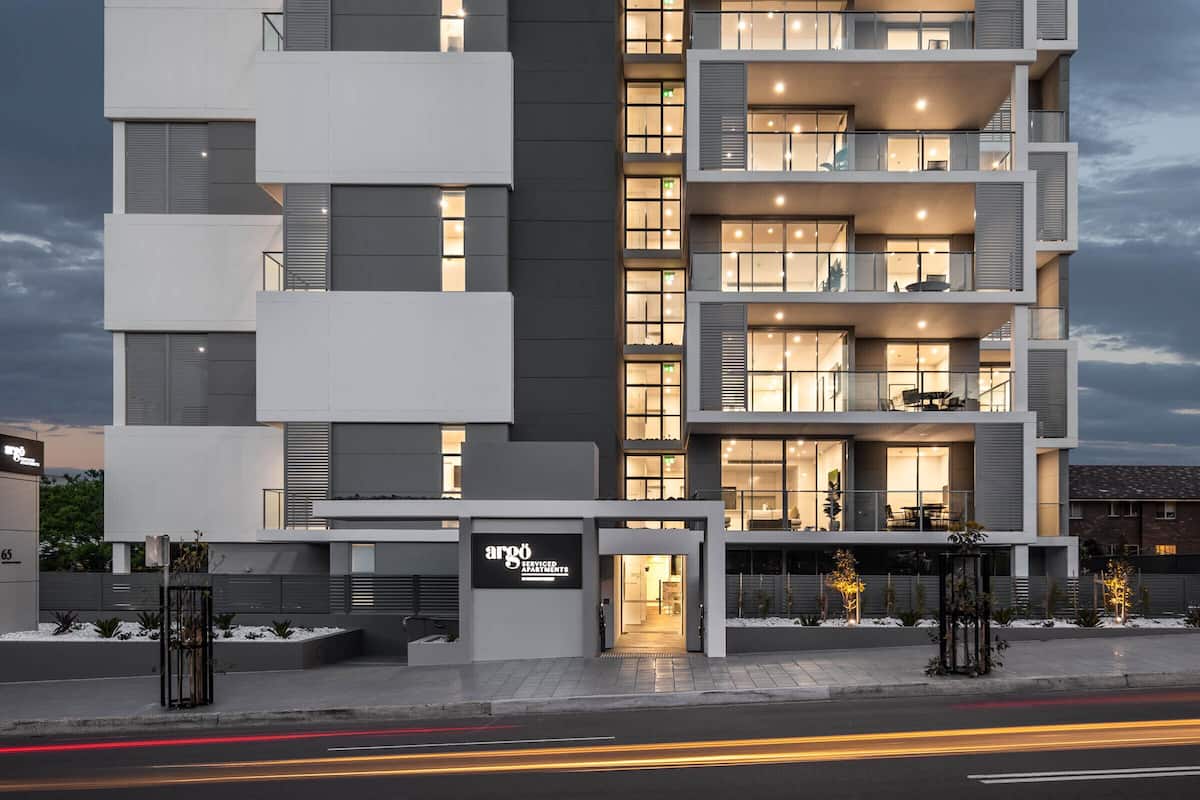 A multi-story modern apartment building with balconies, large windows, and a sign for serviced apartments.