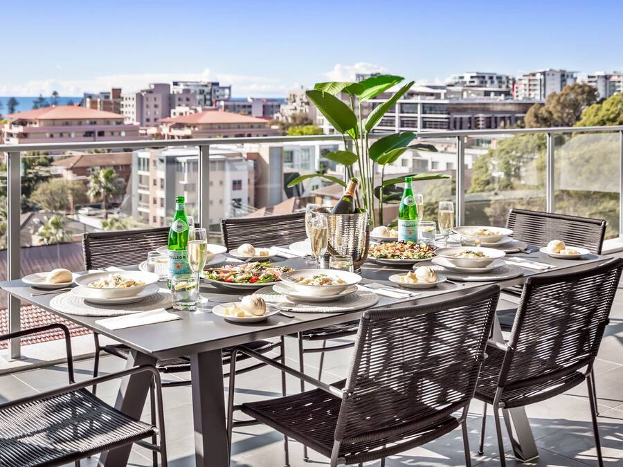 A dining table set outdoors with chairs, a bottle of champagne, and a glass of wine.
