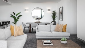A modern living room with two grey sofas, a coffee table, and a dining area with a round table and chairs. - Argo Serviced Apartments (Wollongong)