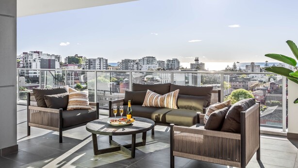 A modern balcony with a sofa set, a round table, and a bottle of champagne. - Argo Serviced Apartments (Wollongong)
