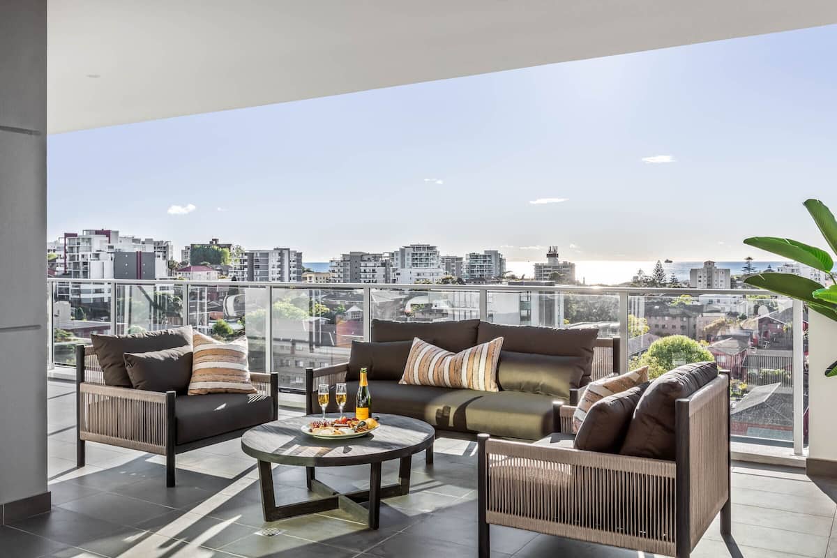 A modern balcony with a sofa set, a round table, and a bottle of champagne.
