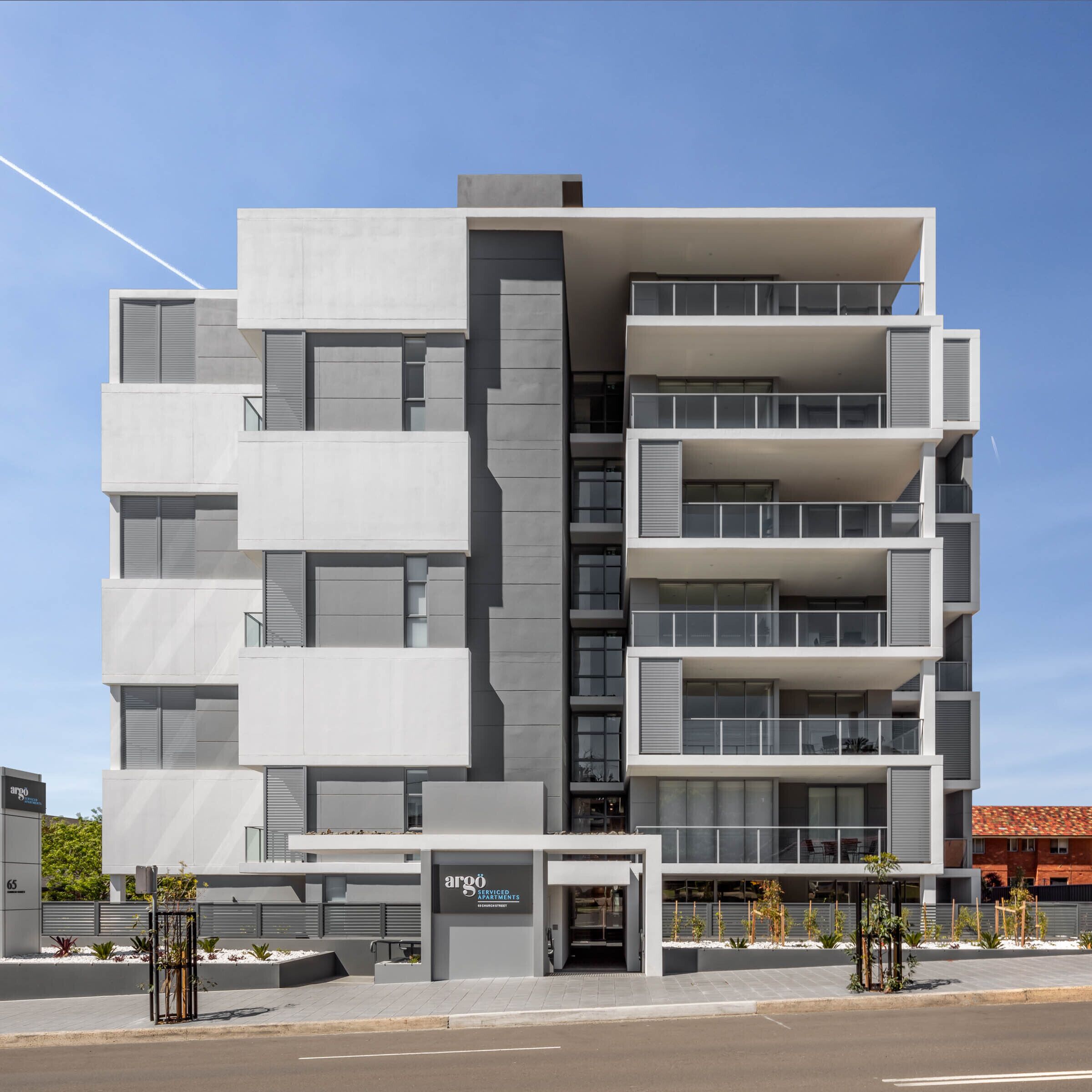 Un immeuble moderne à plusieurs étages, proposant des appartements avec services, doté d’une façade plane, de grandes fenêtres et d’une entrée sécurisée par un portail.