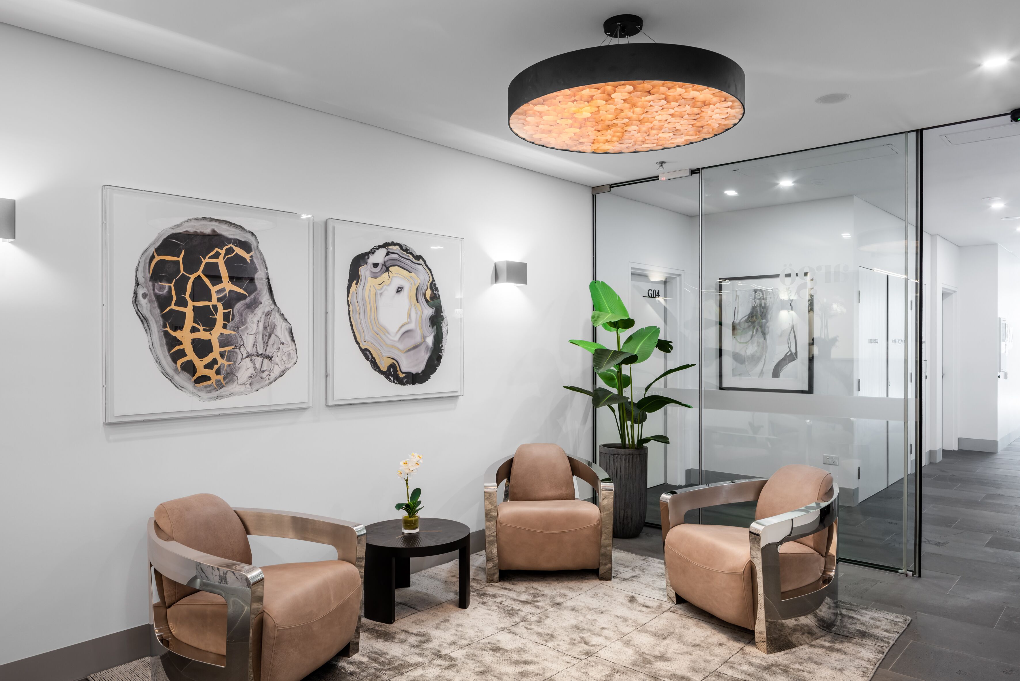 Un hall d’entrée moderne avec trois fauteuils en cuir, une cloison en verre et deux tableaux abstraits accrochés au mur.