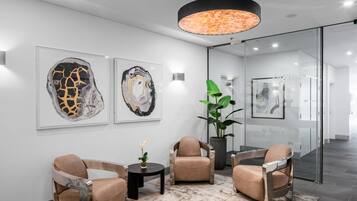 Un hall d’entrée moderne avec trois fauteuils en cuir, une cloison en verre et deux tableaux abstraits accrochés au mur.