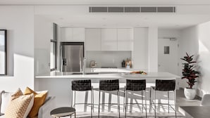 A modern kitchen with a central island, stainless steel appliances, and bar stools. - Argo Serviced Apartments (Wollongong)