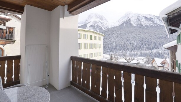 Un balcón con barandilla de madera, una puerta blanca y vistas a montañas nevadas.