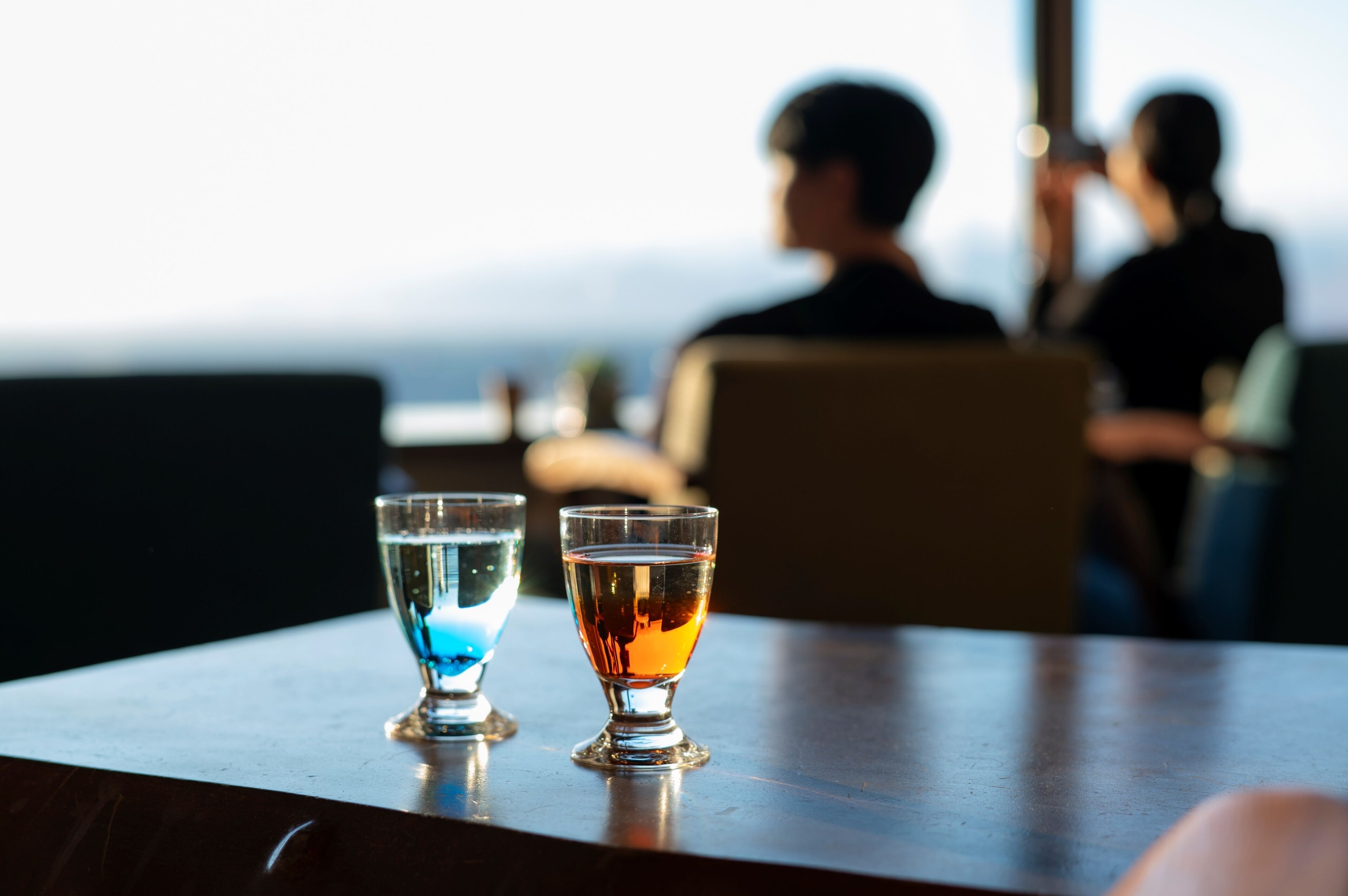 Two glasses on a table with a view of people in the background.
